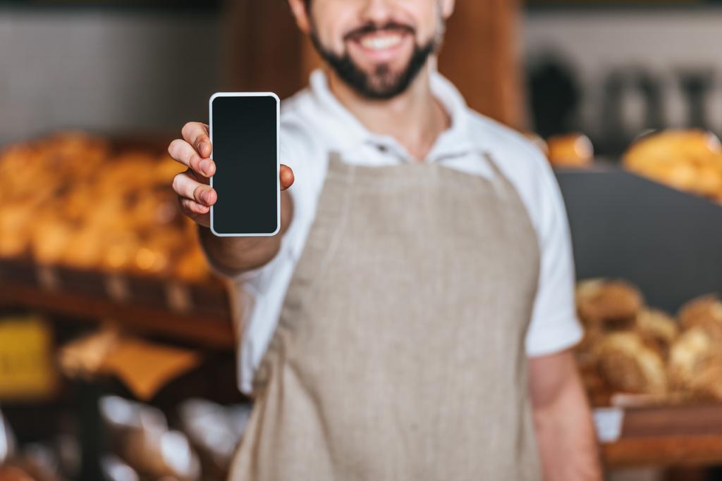 Μερική άποψη της χαμογελαστός υπάλληλος του καταστήματος ΠΑΡΟΥΣΙΑΣΗ smartphone με κενή οθόνη σε σούπερ μάρκετ - Φωτογραφία, εικόνα