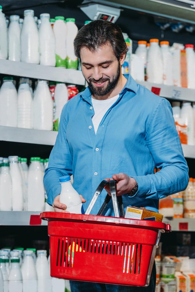 man putting bottle of milk into shopping basket in supermarket - Photo, Image