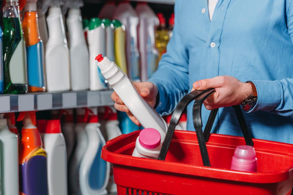 partial view of shopper putting detergent into shopping basket in supermarket - Photo, Image