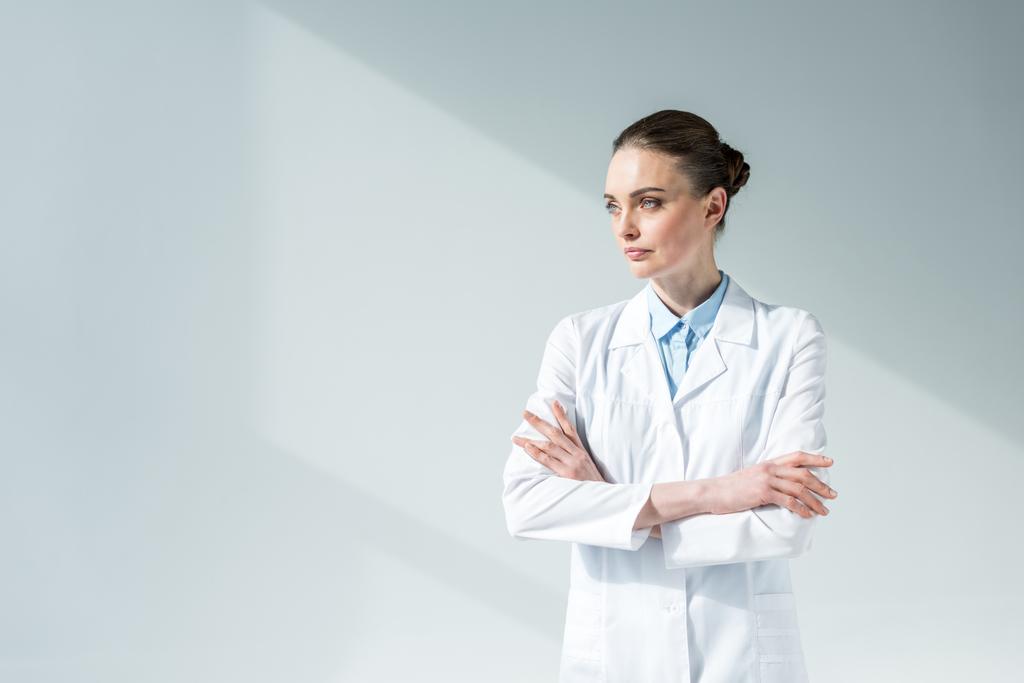 atractiva doctora con brazos cruzados mirando hacia otro lado en gris
 - Foto, Imagen