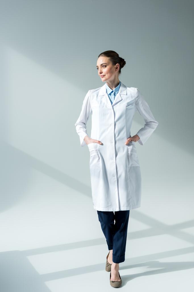 médico femenino serio en bata blanca mirando hacia otro lado en gris
 - Foto, imagen
