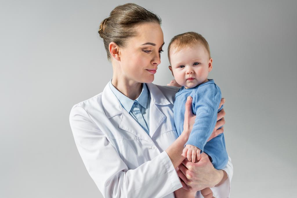 pediatra sonriente sosteniendo a un bebé en gris
 - Foto, Imagen
