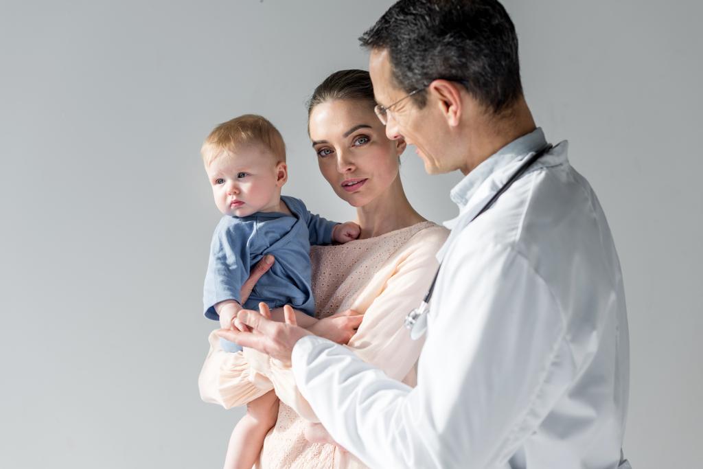 mother showing her little child to pediatrician on grey - Photo, Image