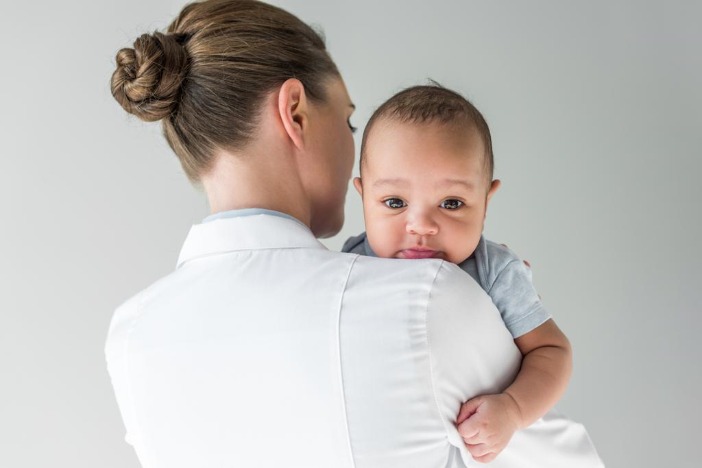 vista trasera de pediatra femenina con bebé afroamericano aislado en gris
 - Foto, Imagen
