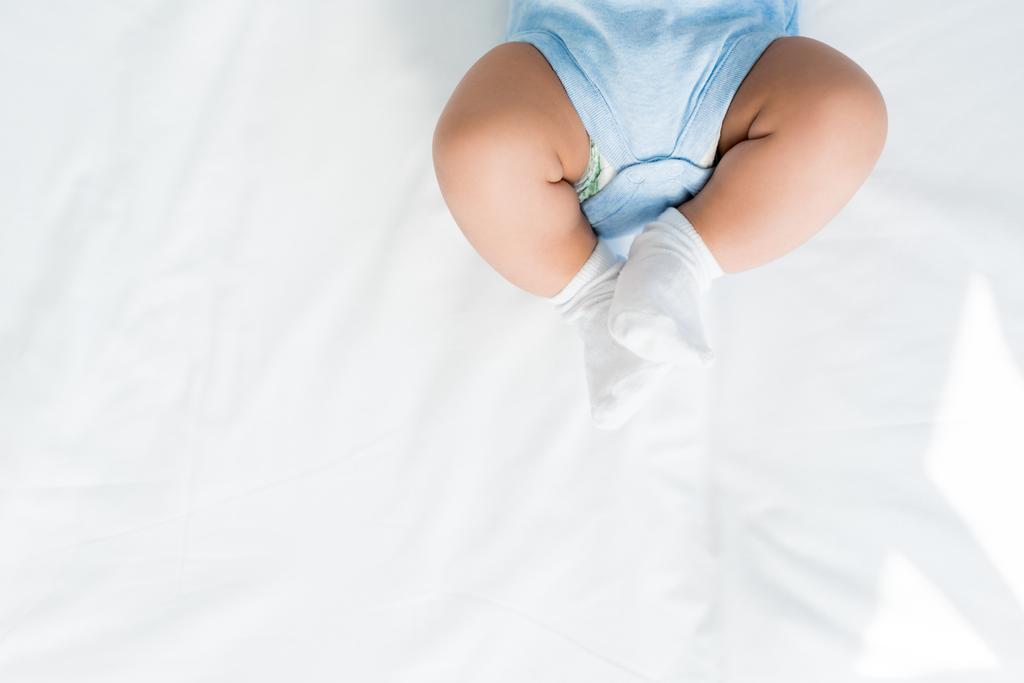recortado tiro de niño pequeño en rompers y calcetines blancos acostado en la cama
 - Foto, imagen