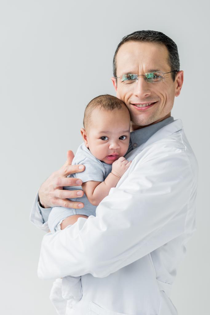 pediatra adulto sorridente segurando pequeno bebê isolado em branco
 - Foto, Imagem
