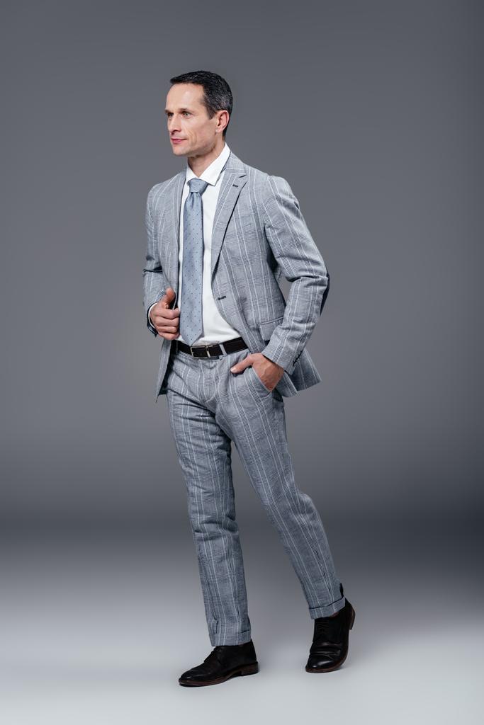 schöner erwachsener Geschäftsmann im eleganten Anzug, der auf grau läuft - Foto, Bild