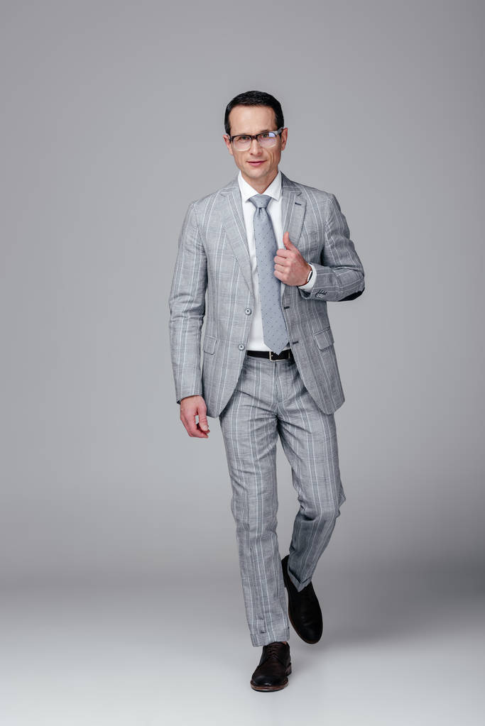stylish adult businessman in grey suit walking at camera on grey - Photo, Image