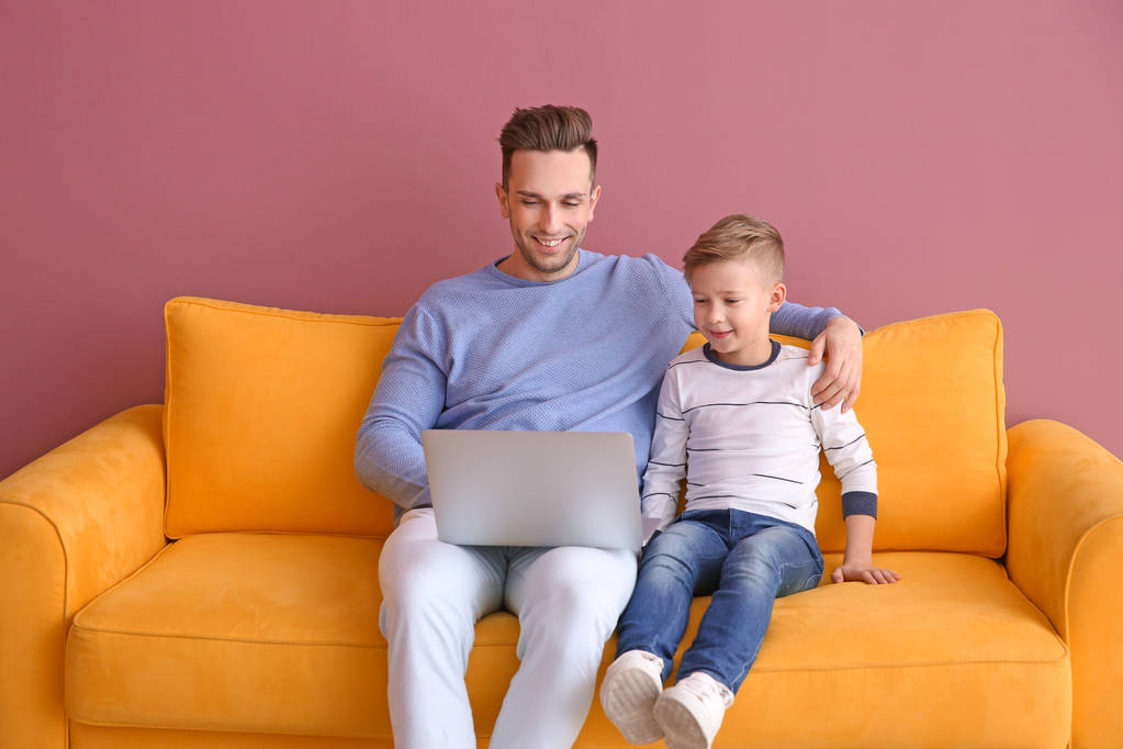 少年と彼の父親、室内のソファーの上に座ってノート パソコンで - 写真・画像
