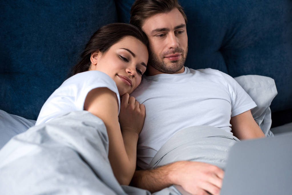 Smiling couple looking at laptop while lying in bed - Photo, Image