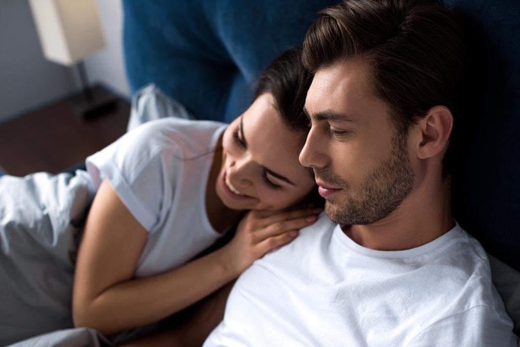 Smiling man and woman tenderly embracing while lying in bed - Photo, Image