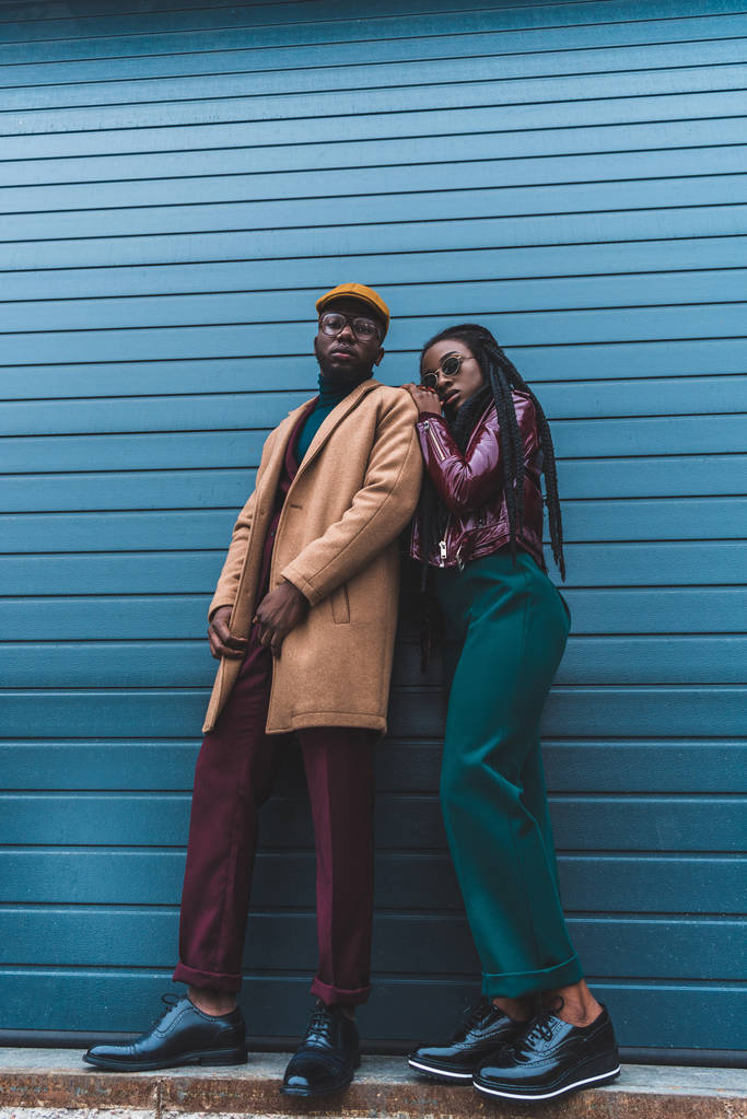 lage hoekmening van stijlvolle Afrikaanse Amerikaanse echtpaar camera kijken terwijl poseren samen op straat - Foto, afbeelding