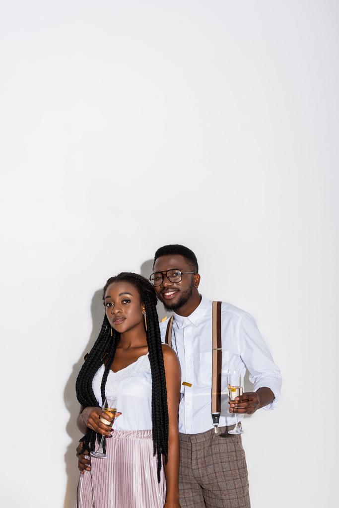stylische junge afrikanisch-amerikanische Paar hält ein Glas Champagner und lächelt in die Kamera auf weiß - Foto, Bild