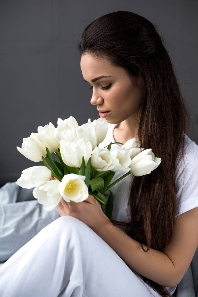 Mulher atraente sentado na cama e segurando buquê de tulipas
 - Foto, Imagem