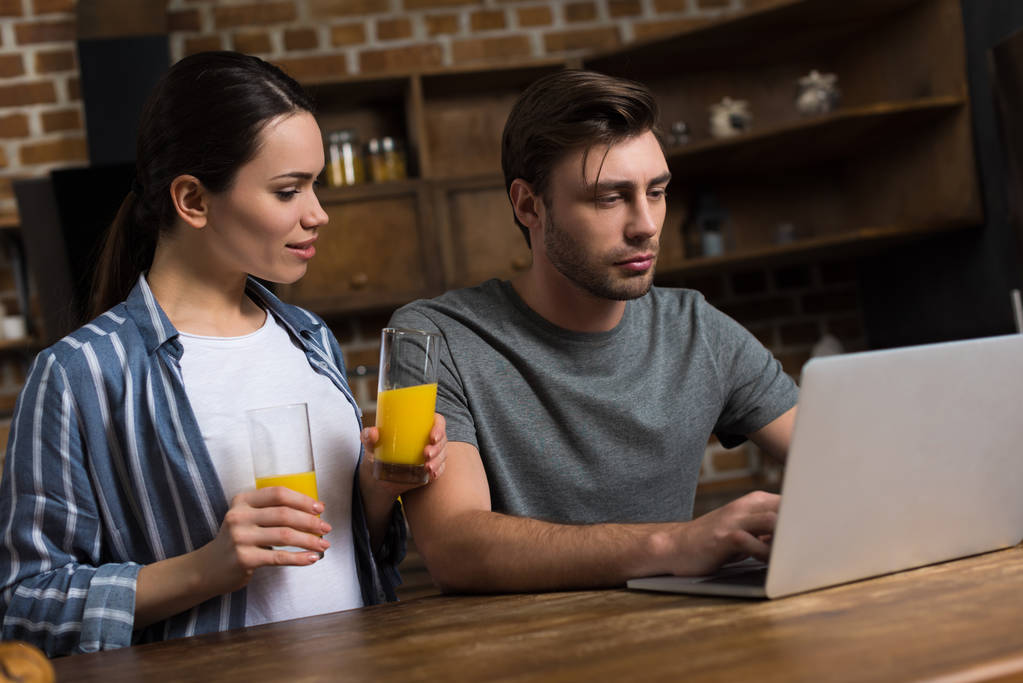 Wife offering juice to her husband working at laptop - Photo, Image