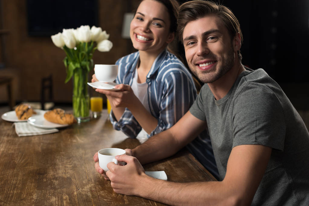 Χαμογελαστή γυναίκα και άντρα που πίνει καφέ στην κουζίνα - Φωτογραφία, εικόνα