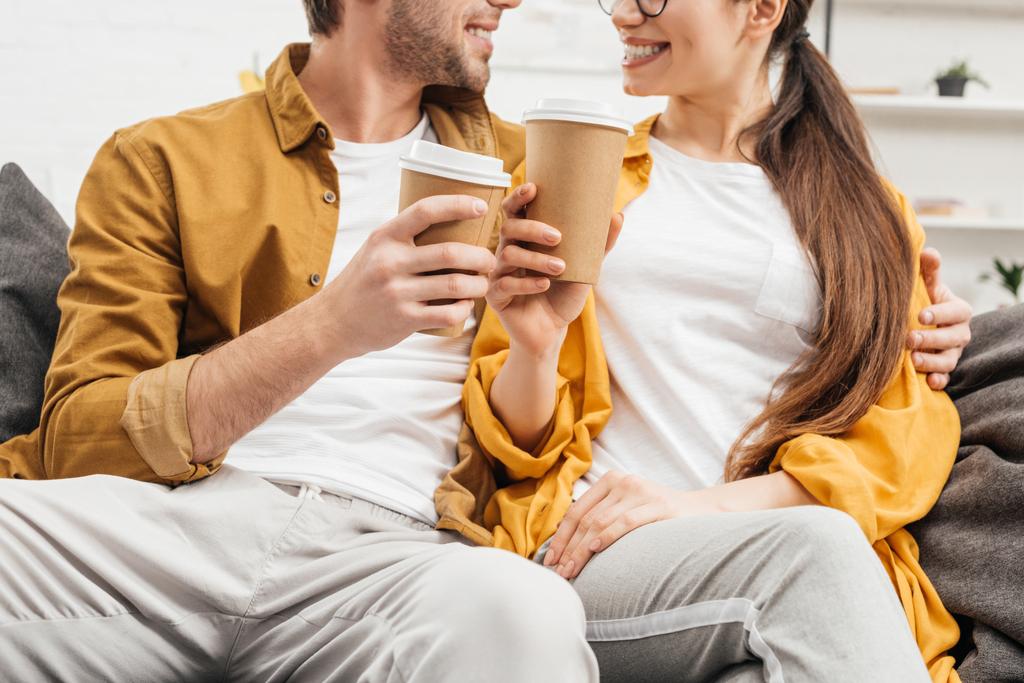 tiro cortado de flertar casal e copos de papel clinking de café no sofá
 - Foto, Imagem