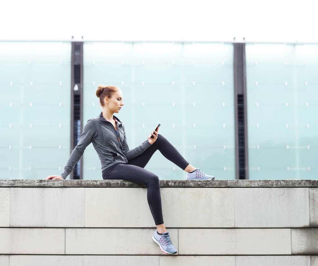 Femme jeune, en forme et sportive assise sur une frontière en béton. Fitness, sport, jogging urbain et mode de vie sain concept
. - Photo, image