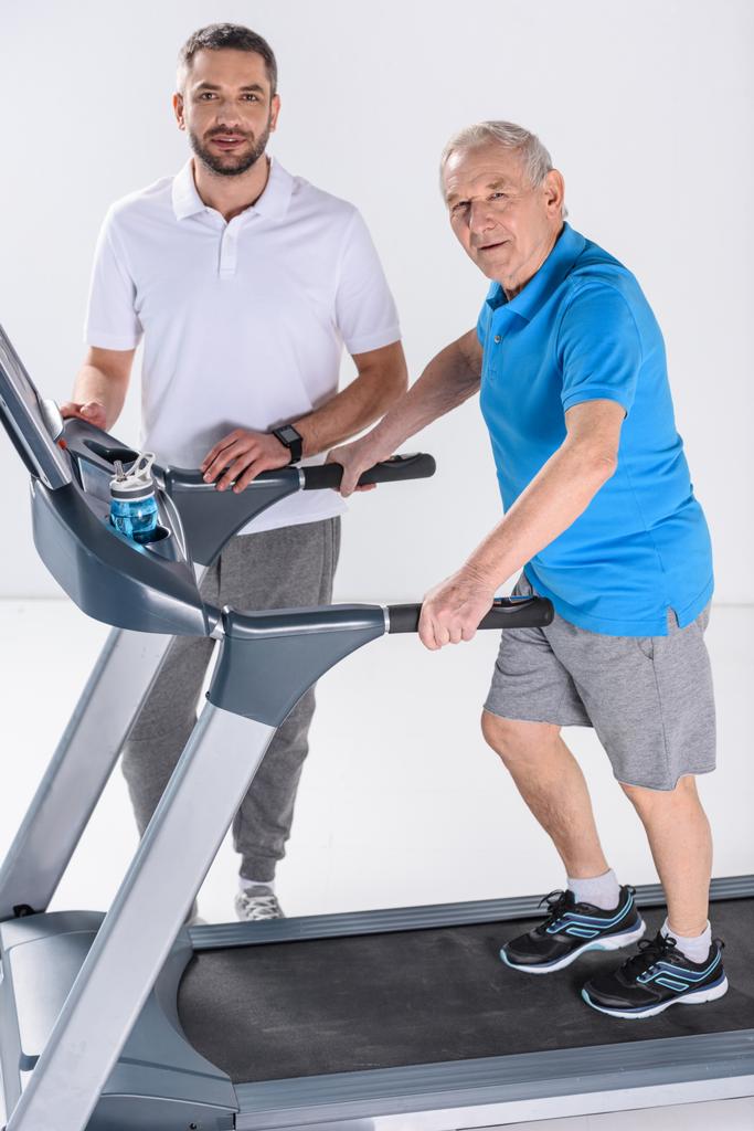 реабілітаційний терапевт і старший чоловік на біговій доріжці ізольовані на сірому
 - Фото, зображення