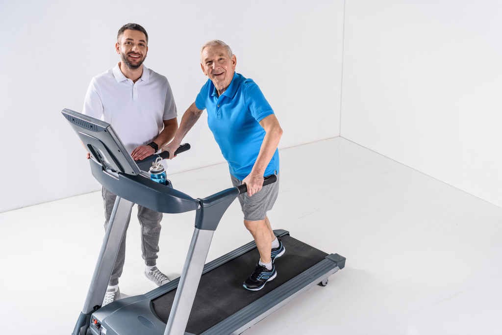 high angle view of rehabilitation therapist assisting senior man exercising on treadmill  - Photo, Image