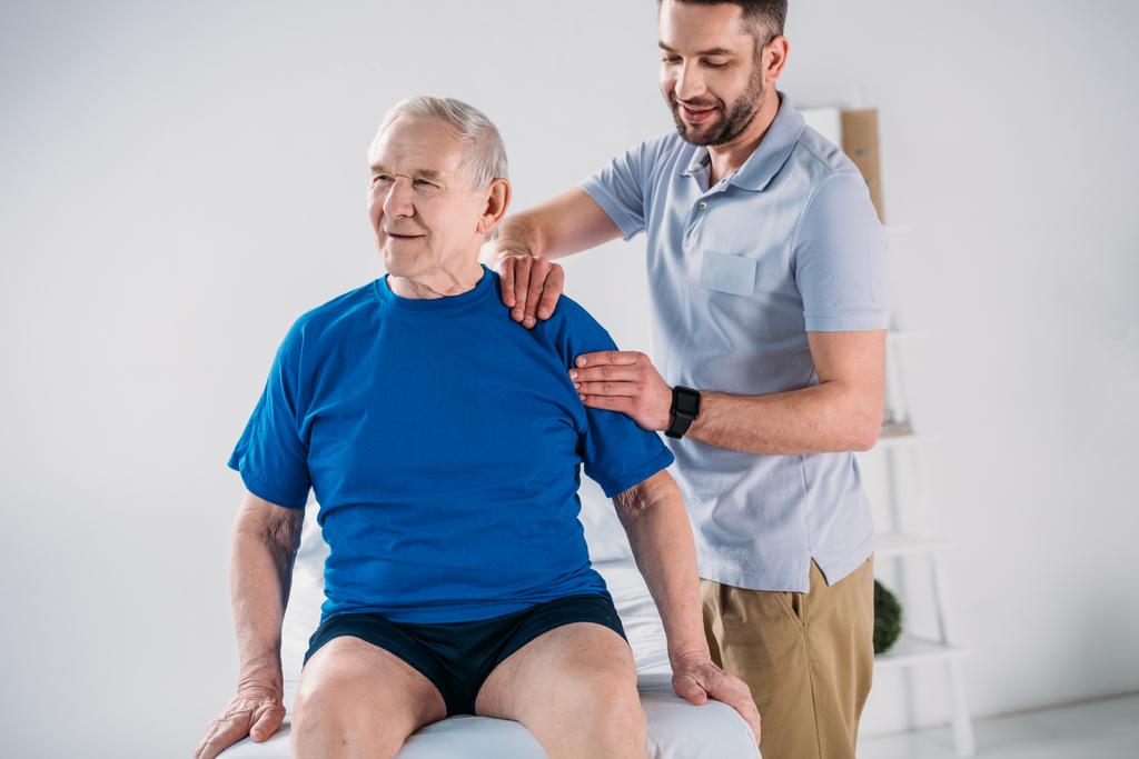 ritratto del fisioterapista che fa massaggio all'uomo anziano sul tavolo da massaggio
 - Foto, immagini