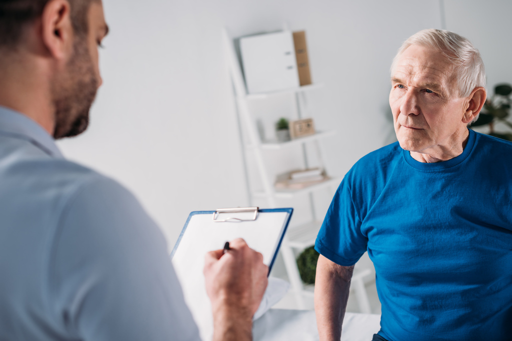 vista parziale del terapeuta riabilitativo con blocco note e uomo anziano
 - Foto, immagini