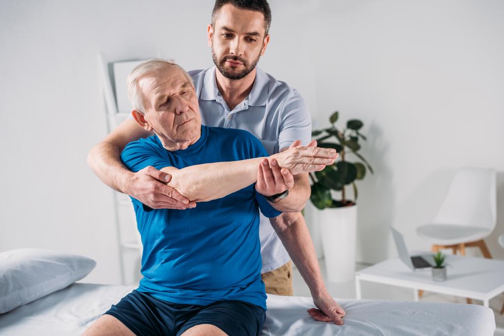 Porträt eines Physiotherapeuten, der einem älteren Mann auf einem Massagetisch massiert - Foto, Bild