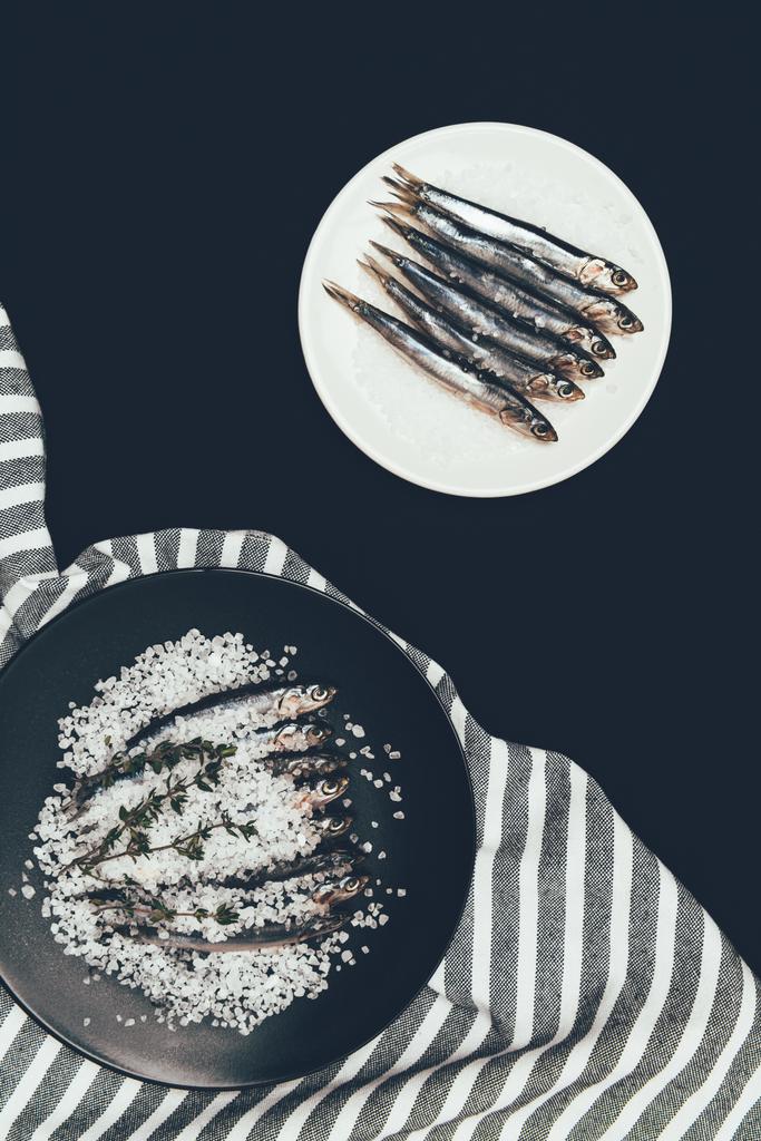 Gezouten stapel van gezouten vis met rozemarijn in de koekenpan en plaat met vis geïsoleerd op zwart - Foto, afbeelding