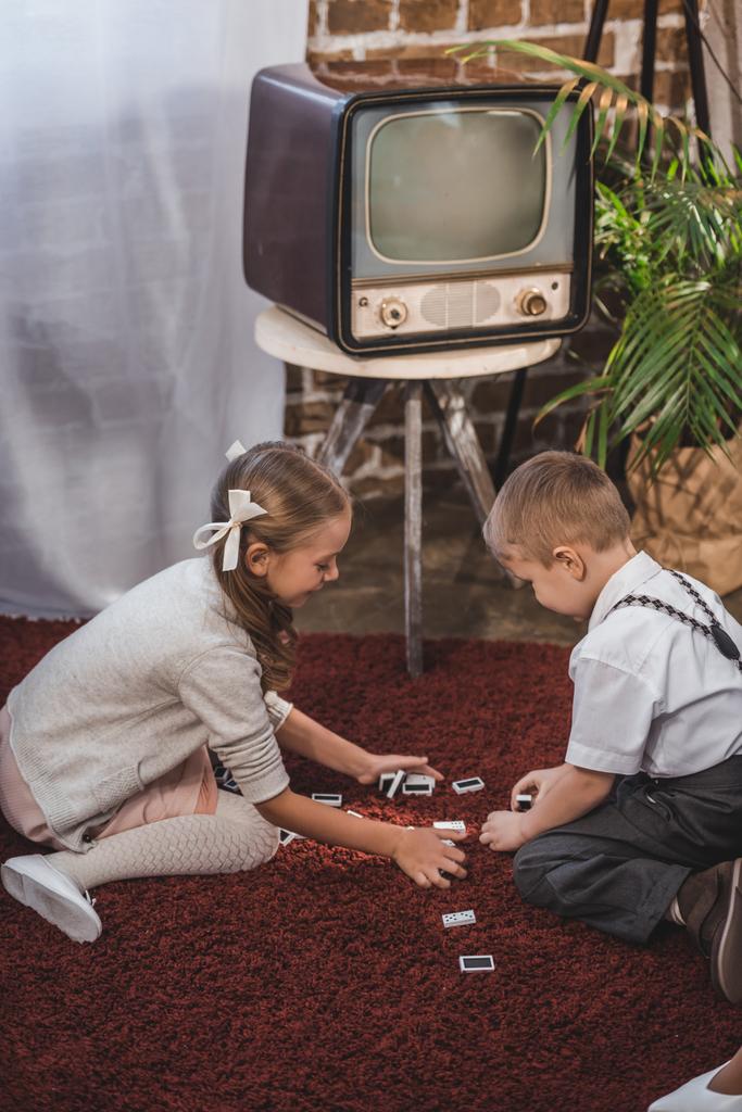 vista lateral de niños lindos jugando dominó juntos en casa, estilo de 1950
 - Foto, Imagen
