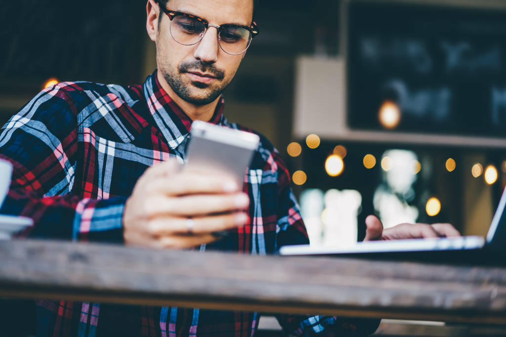 最新のネットブックでフリーランスのコピー ライターを働いている流行に敏感な人の画像をトリミング読みながらコンピューターを受け取ったコーヒー店内で座っていると、4 g を使用してデジタル電話デバイスで sms メッセージ - 写真・画像
