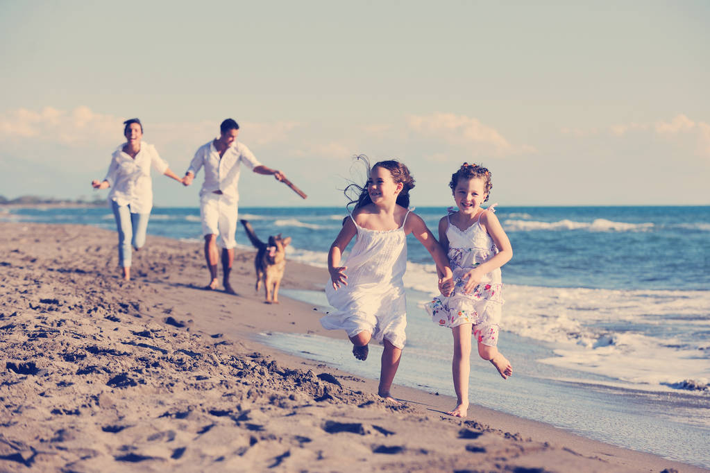 boldog fiatal család fehér ruhában érezze jól magát, és játszani gyönyörű kutya nyaralás gyönyörű strandon  - Fotó, kép