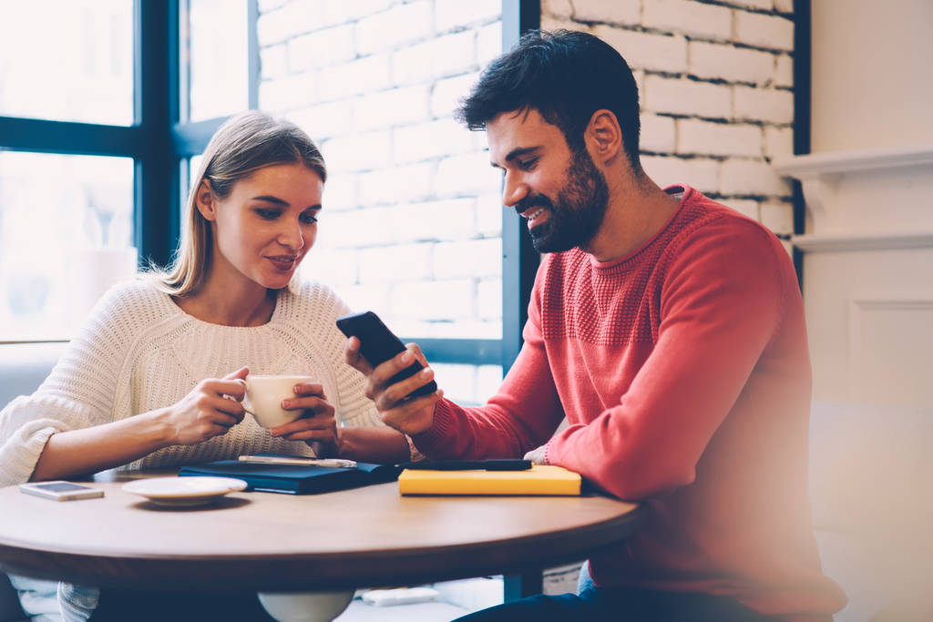 Uśmiechający się romantyczna para oglądając film na smartfon jednocześnie ciesząc się spędzać czas razem na przerwę na kawę, brodaty facet pokazując zdjęcia na telefonie do jego Ładna dziewczyna komunikuje się podczas dnia - Zdjęcie, obraz