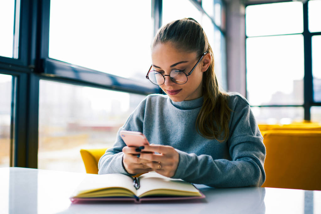 Nuori houkutteleva nainen kutoma viestin avulla hänen moderni älypuhelin istuessaan kahvilassa sisustus, kaunis nuori nainen chattailuun ystävien kautta sovelluksen nykyaikainen matkapuhelin
 - Valokuva, kuva