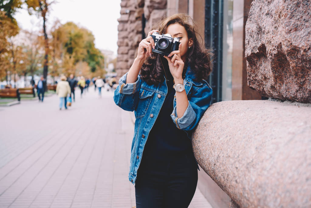Професійний випадково одягнений фотограф робить фотографії на міських обстановках під час прогулянки на вулиці, молода хіпстерська дівчина в джинсовій куртці і кучеряве волосся проводить час на хобі за допомогою старовинної камери
 - Фото, зображення