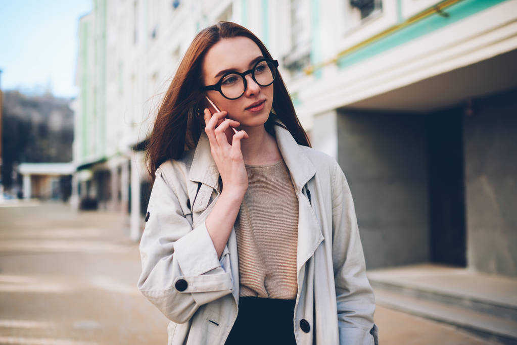 Menina hipster adolescente atraente desfrutando de primavera tempo ensolarado passeando em cenários urbanos fundo ter conversa telefônica, jovem turista usando conexão em roaming para fazer chamadas móveis
 - Foto, Imagem