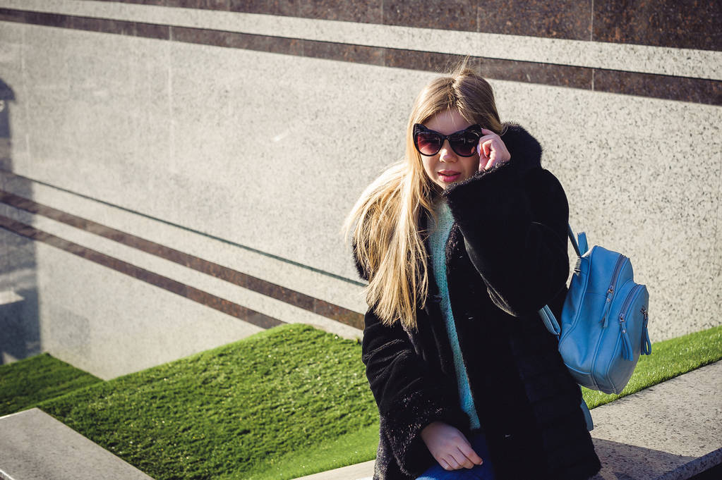 молодая женщина в шубе, свитере и модных солнцезащитных очках с ушами, прогуливается по городу с рюкзаком. Уличная мода
 - Фото, изображение