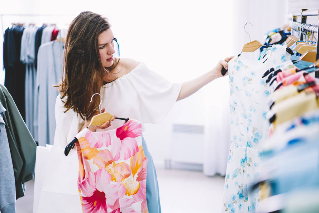 Vonzó trendi öltözött női ügyfél fekszenek segítségével illeszkedő koncepció, míg választott a ruhát vásárol. Professzionális fodrász vásárló divatos megjelenés létrehozása koncentrált tervező boltban kiválasztása - Fotó, kép