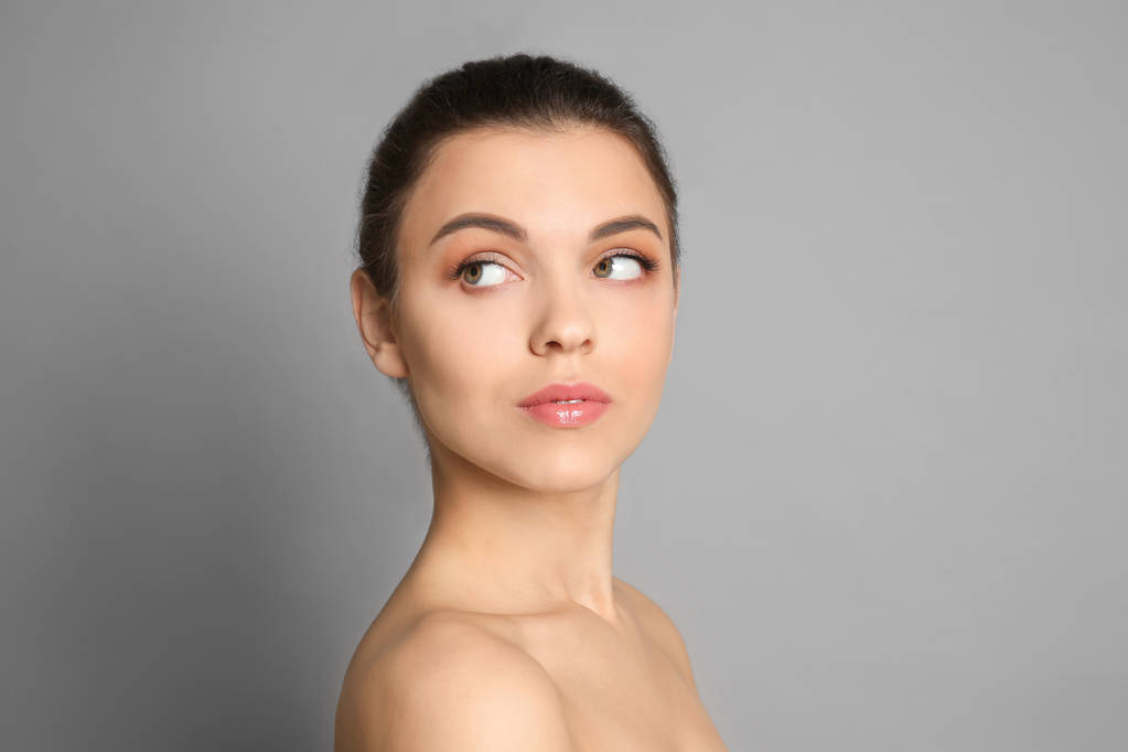Mujer joven con hermoso maquillaje sobre fondo gris. Productos cosméticos profesionales
 - Foto, imagen