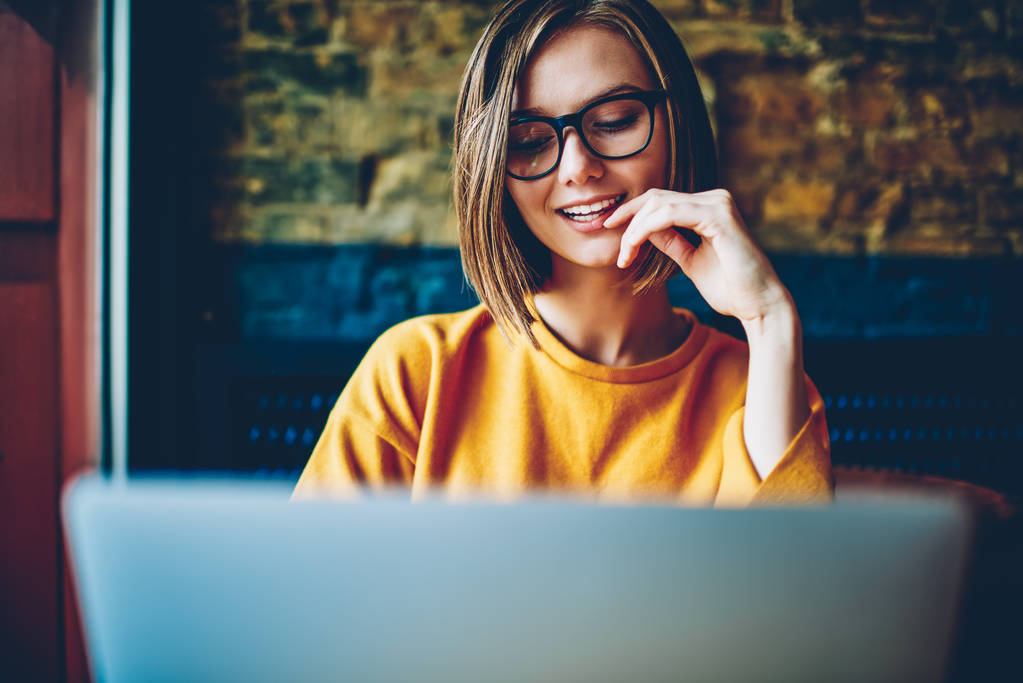 Joyeux étudiant attrayant féminin avec des lunettes et une coupe de cheveux courte bavarder en ligne dans les réseaux sociaux avec un ami sur l'ordinateur moderne en utilisant une connexion Internet haut débit gratuit assis dans un café
 - Photo, image