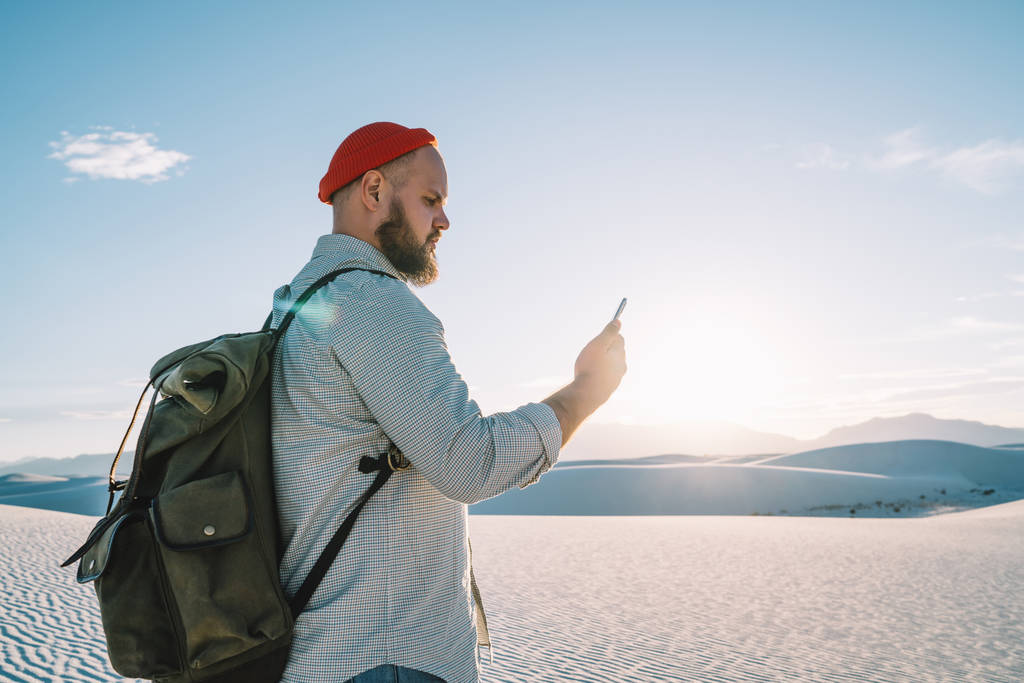 junger Hipster überprüft Anwendungsbenachrichtigung, navigiert per Smartphone und guter mobiler Datenverbindung in der Wüste mit weißem Sand, männlicher Reisender erkundet Landschaften mit Internet beim Roaming - Foto, Bild