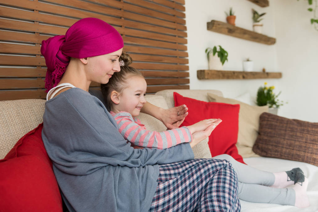 Jeune femme adulte cancéreuse passer du temps avec sa fille à la maison, se détendre sur le canapé. Cancer et concept de soutien familial
. - Photo, image