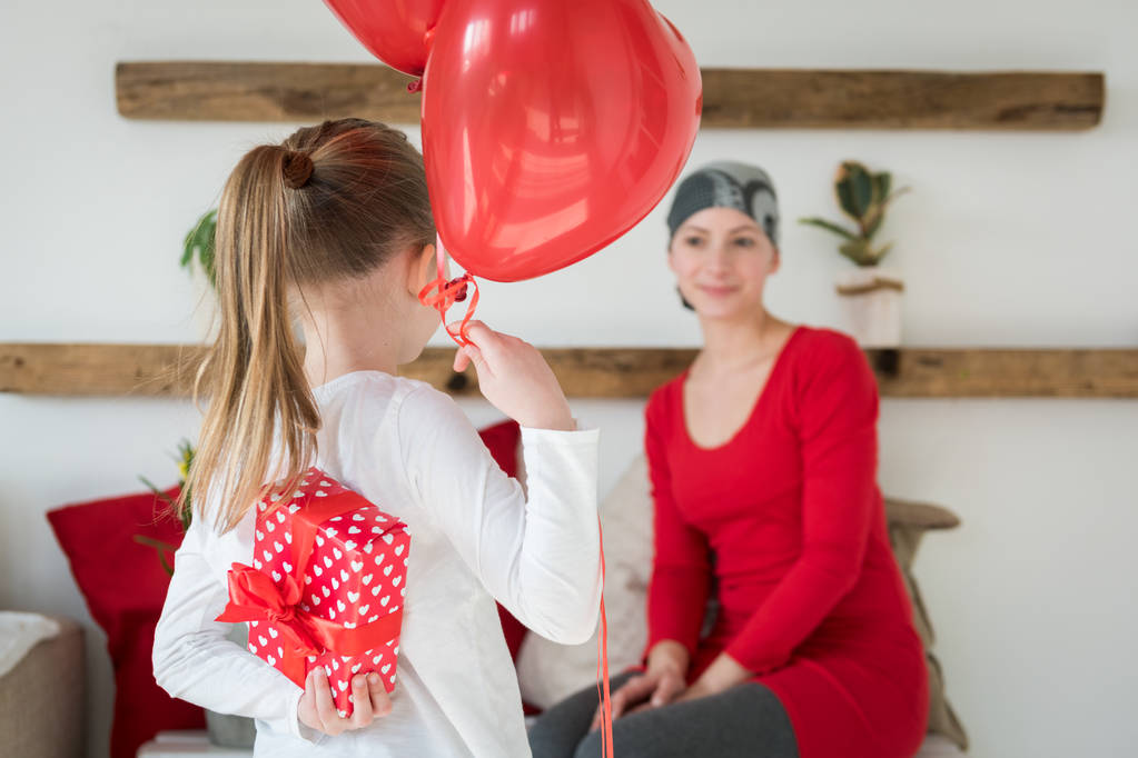 Die junge Mutter, Krebspatientin, und ihre süße Tochter feiern die Heimkehr aus dem Krankenhaus. Willkommen zu Hause oder Geburtstagsfeier mit Luftballons und Geschenken. - Foto, Bild
