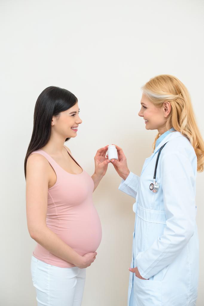 Geburtshelfer Gynäkologe und schwangere Frau hält Glas mit Pillen - Foto, Bild