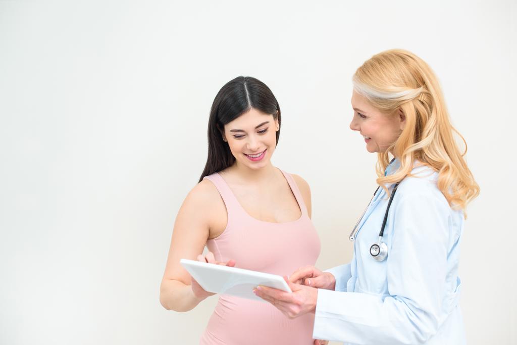 smiling obstetrician gynecologist and pregnant woman using tablet together - Photo, Image