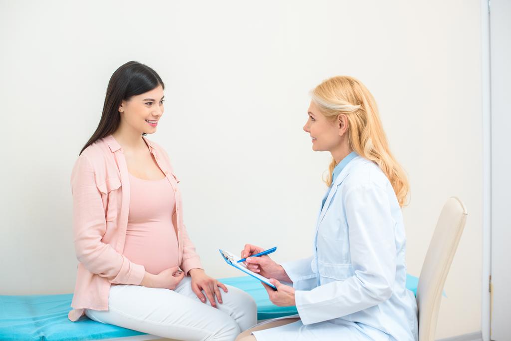ginecologista obstetra consulta mulher grávida na clínica e escrita em prancheta
 - Foto, Imagem