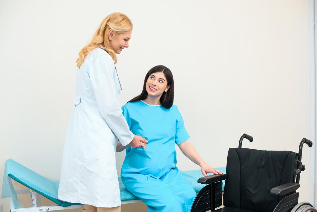 ginekolog położnik, pomagając w ciąży kobiety, aby dostać się do wózka inwalidzkiego - Zdjęcie, obraz