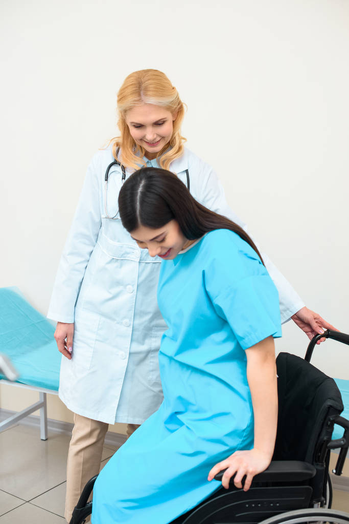 акушер-гинеколог помогает беременной женщине сесть на инвалидное кресло
 - Фото, изображение