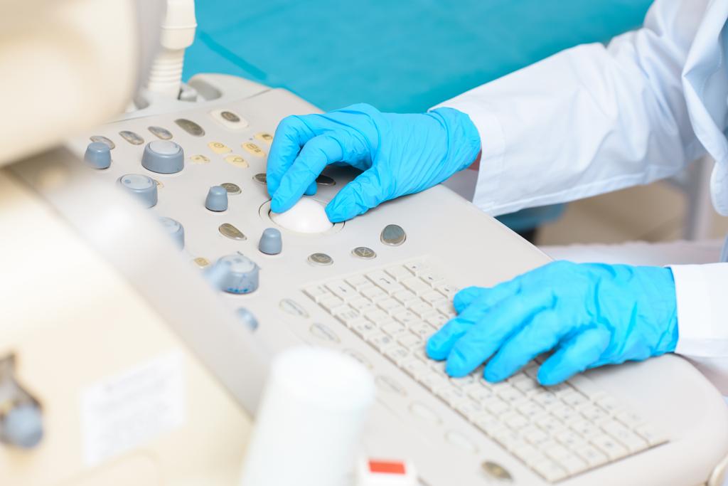 обрезанный снимок акушера-гинеколога в синих перчатках, работающего с ультразвуковым сканером
 - Фото, изображение
