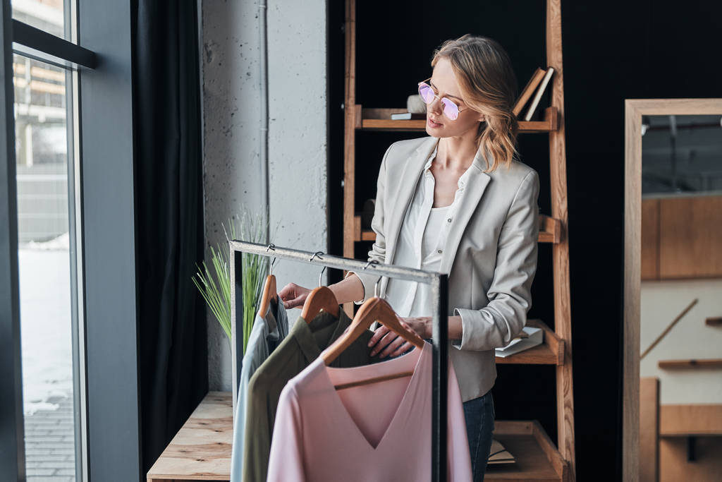 mulher loira escolhendo roupas de classificação, enquanto em pé na oficina
 - Foto, Imagem