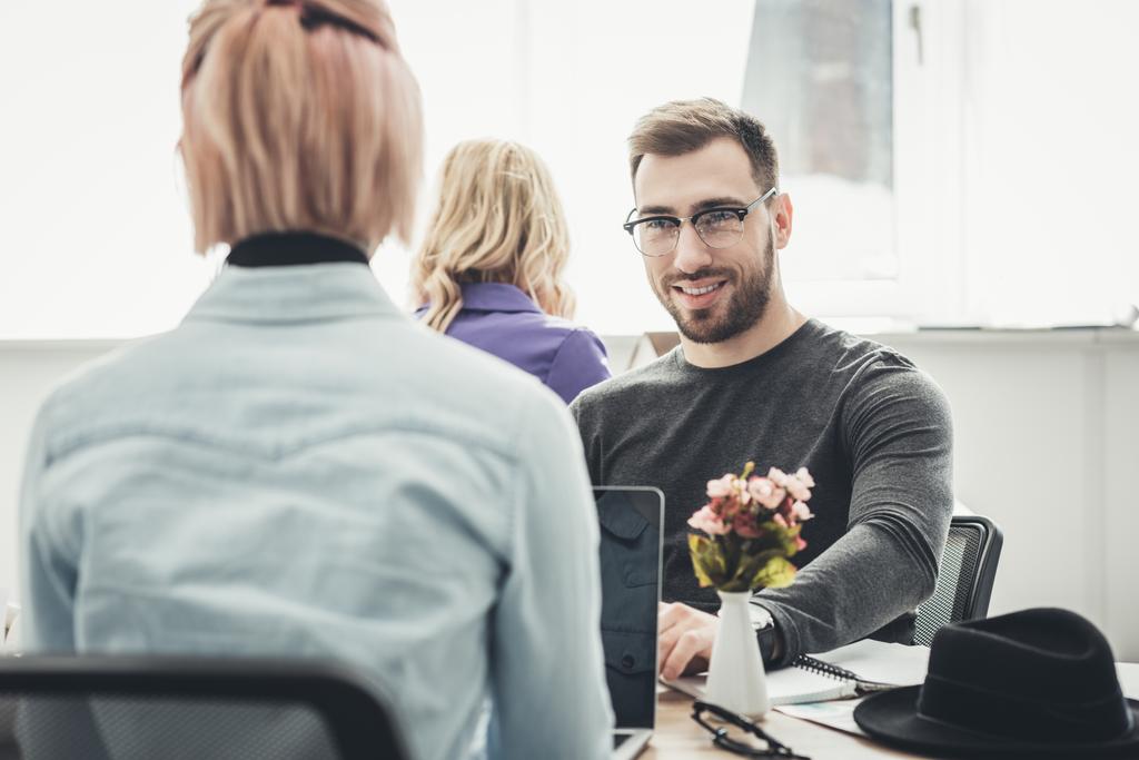 επιλεκτική εστίαση του χαμογελώντας επιχειρηματία σε γυαλιά στο χώρο εργασίας στο γραφείο - Φωτογραφία, εικόνα